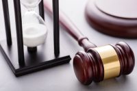 High-angle close-up view of hourglass with white sand pouring and wooden auction or court gavel with copy space on gray background